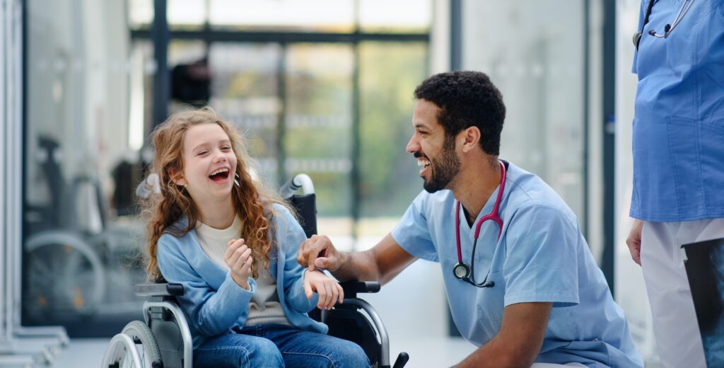 Young multiracial doctor having fun with little girl on wheelchair.